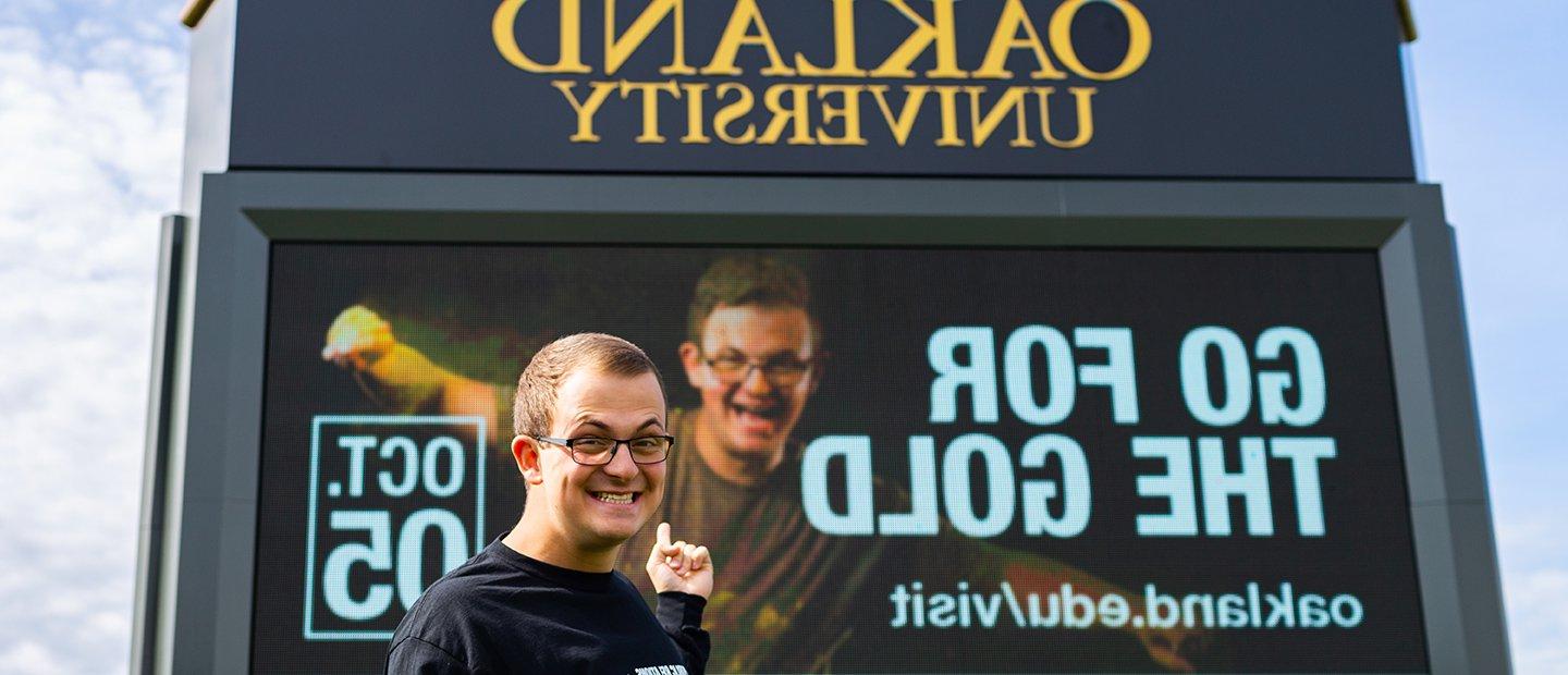 Young man pointing to an ad that he is featured in on an 365英国上市官网 electronic marquee.
